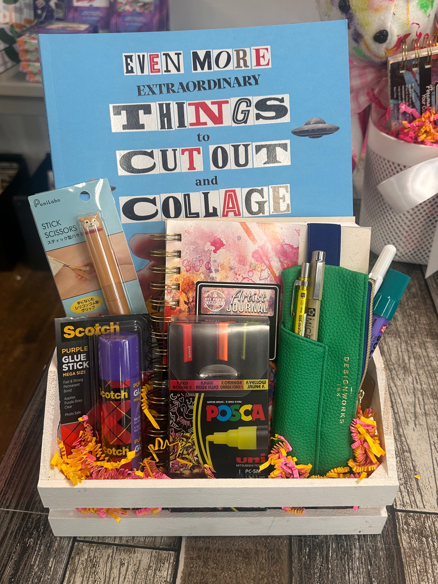 Gift box with art supplies including markers, scissors, and a collage book on a wooden surface.