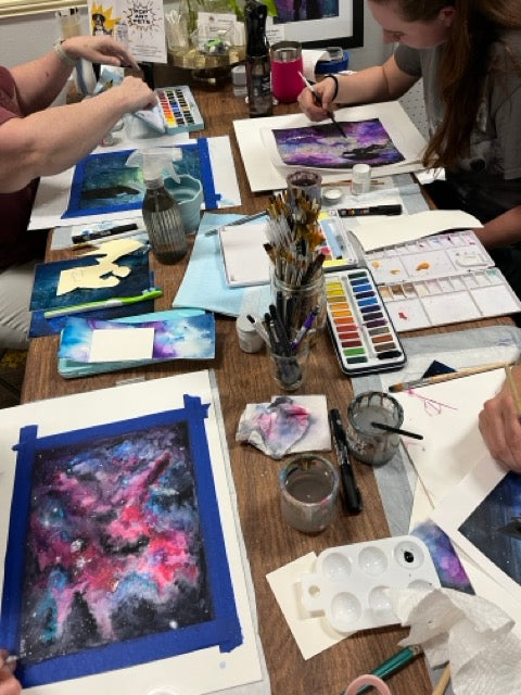 Artistic workshop with participants painting abstract artworks on a table.