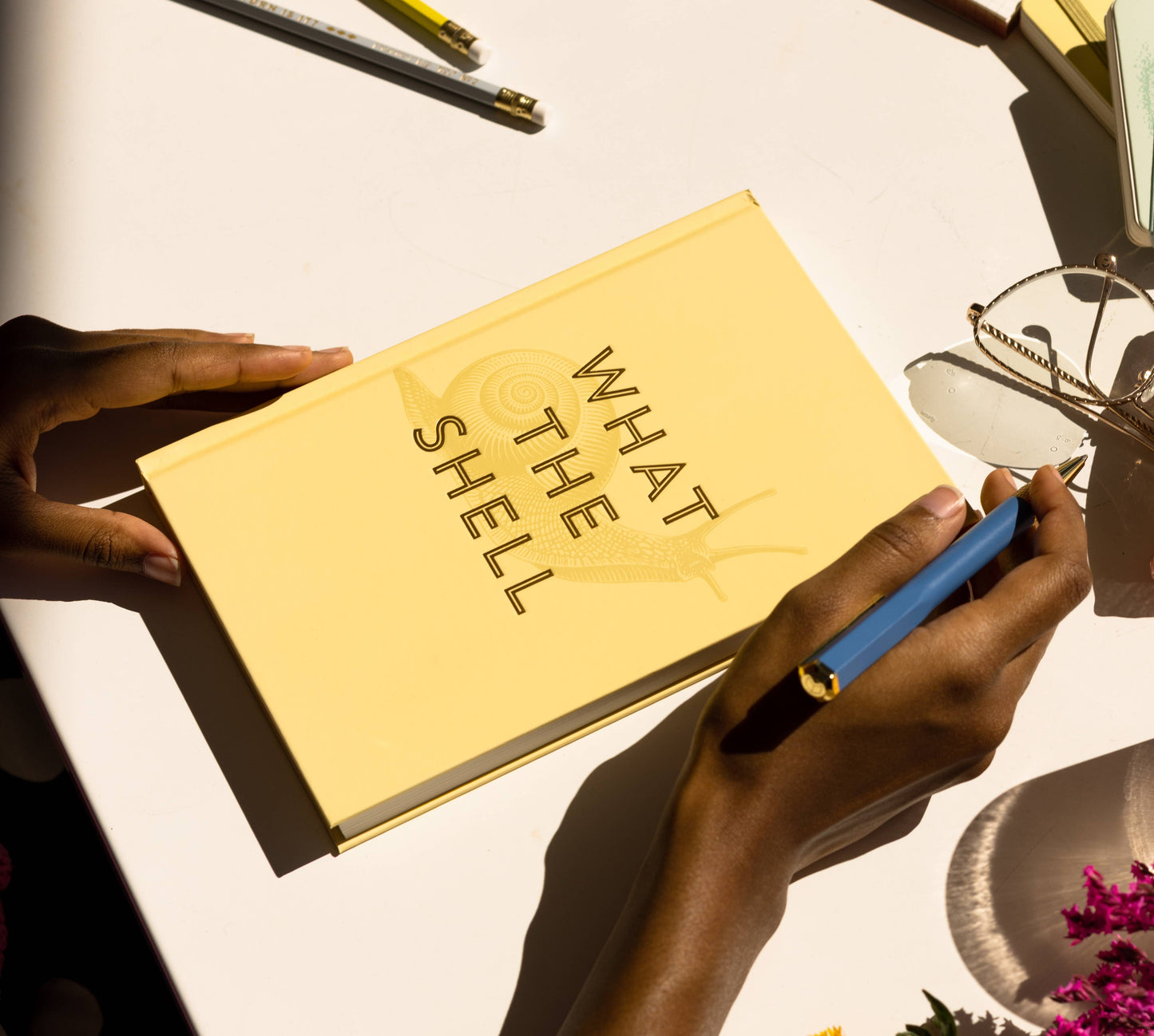Book titled 'What The Shell' held by a person with a pen on a light surface.
