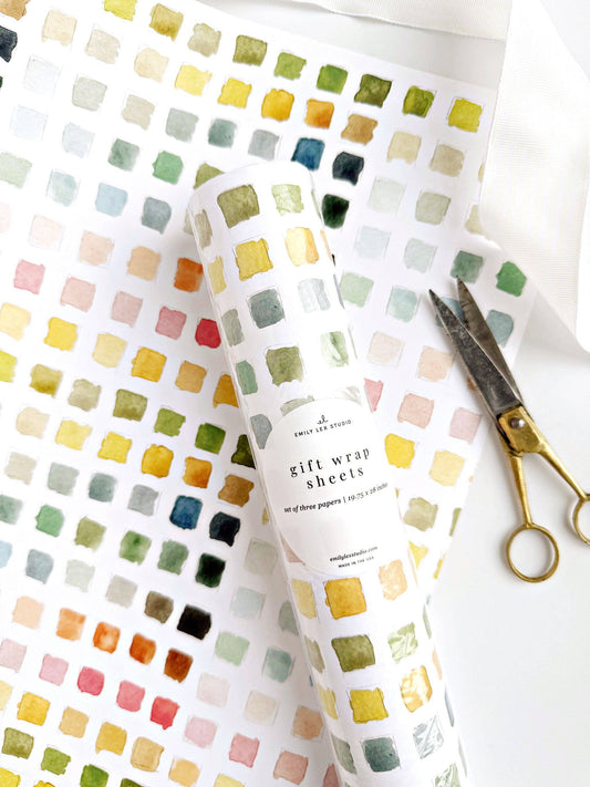 Colorful square patterned gift wrap sheets with a pair of scissors on a white background