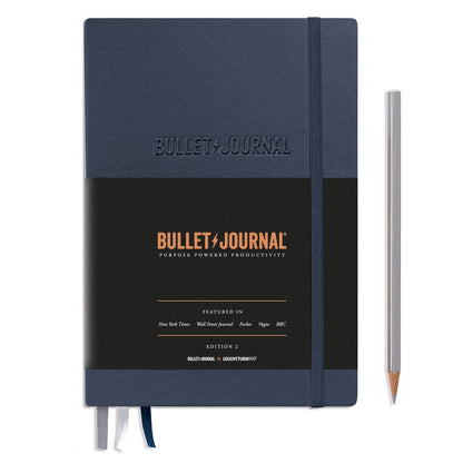 Blue and black bullet journal with a pencil on a white background