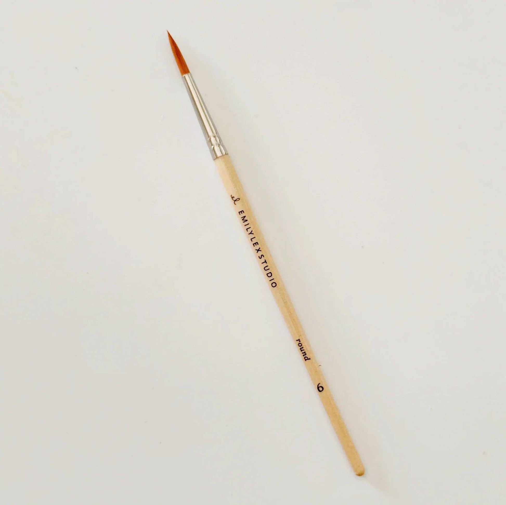 Paintbrush with wooden handle and gold ferrule on a light gray background