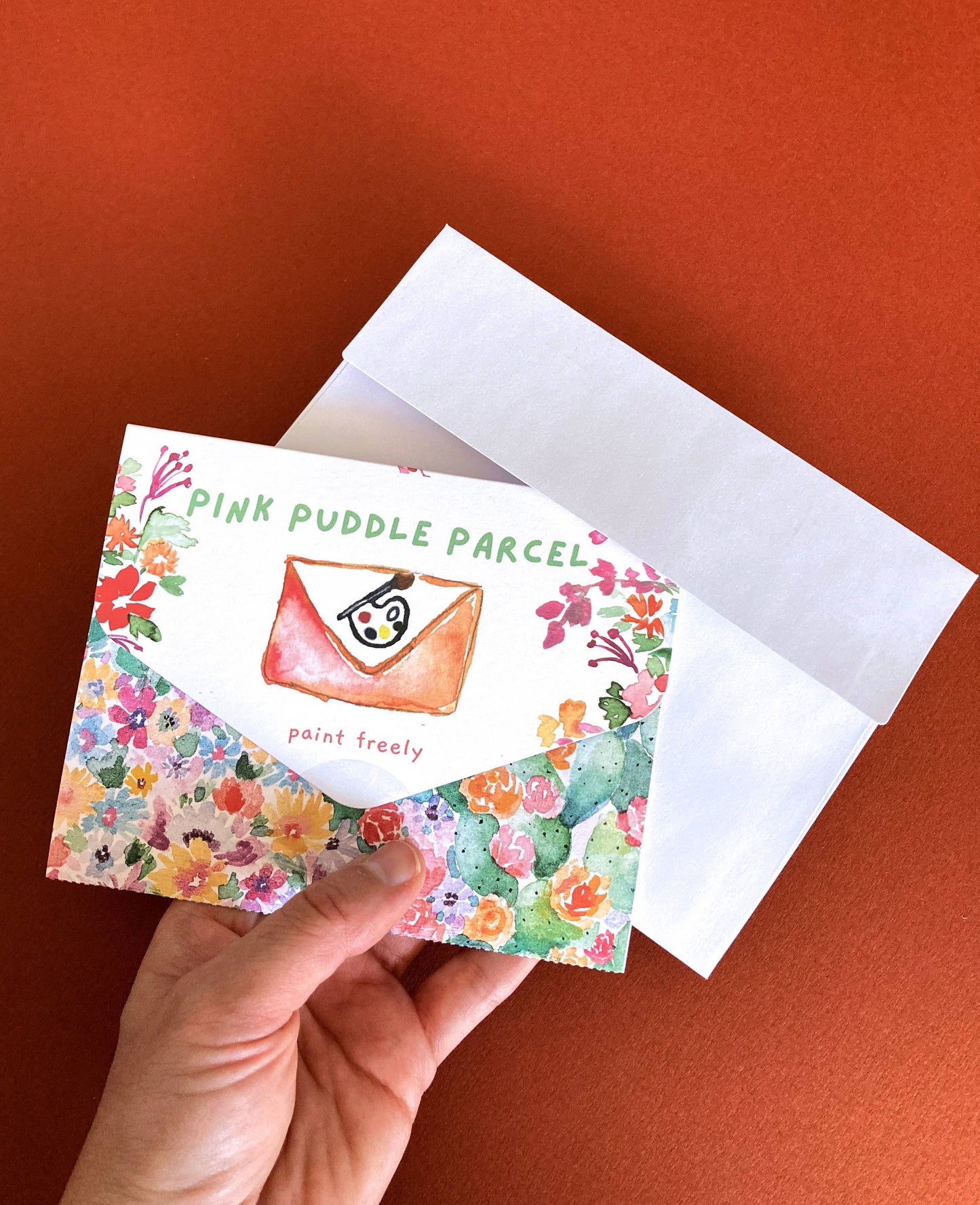 Floral card with 'Pink Puddle Parcel' branding held by a hand on an orange background