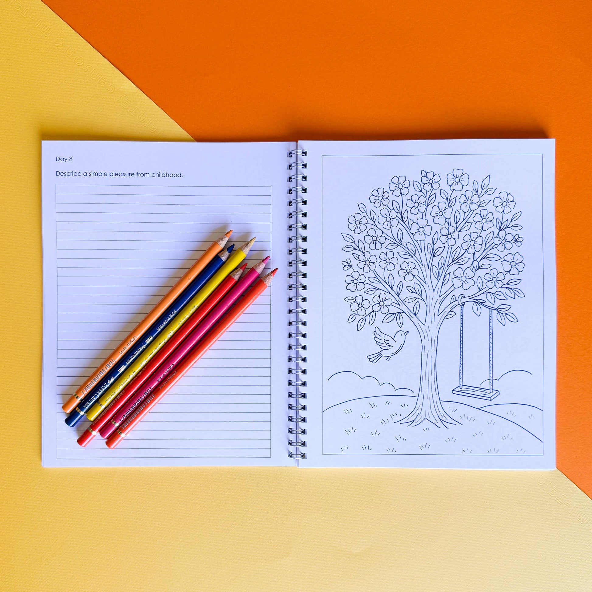 Open notebook with lined pages and coloring page of a tree with a swing on an orange and yellow gradient background.
