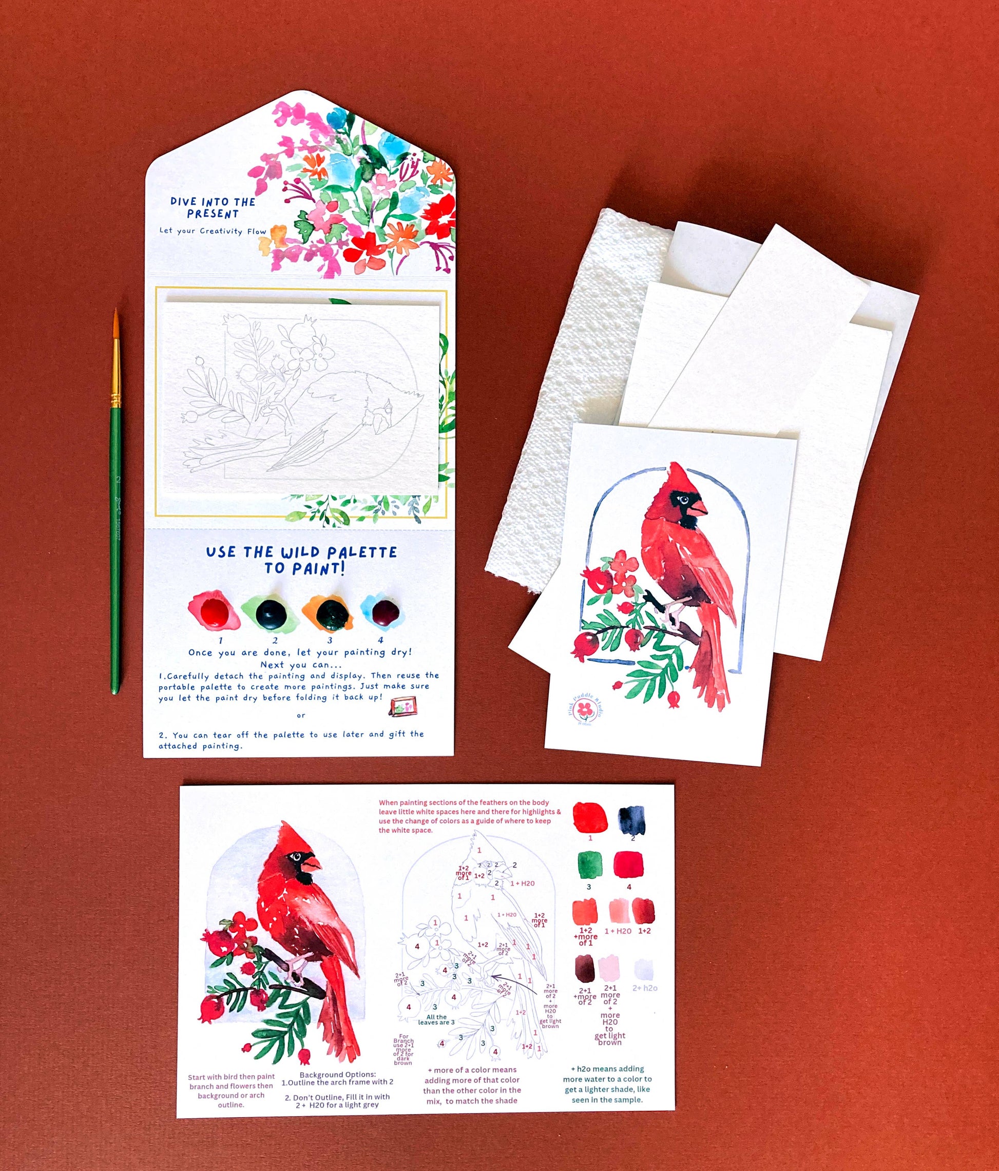 Cardinal-themed art set with cards, paint palette, and brush on a red background