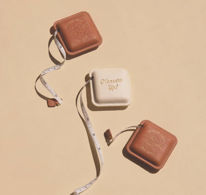 Brown and beige measuring tape with 'Measure Up!' text on a beige background