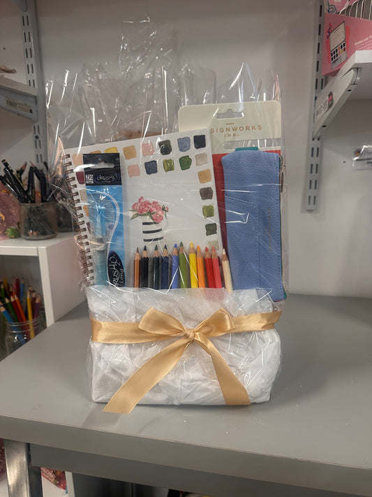 Packaged art supplies with a gold ribbon on a gray surface