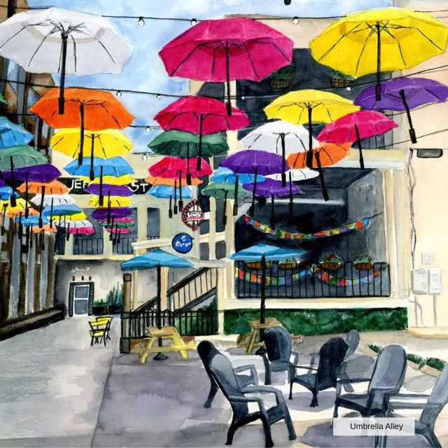 Colorful umbrellas above a street scene with buildings and people.