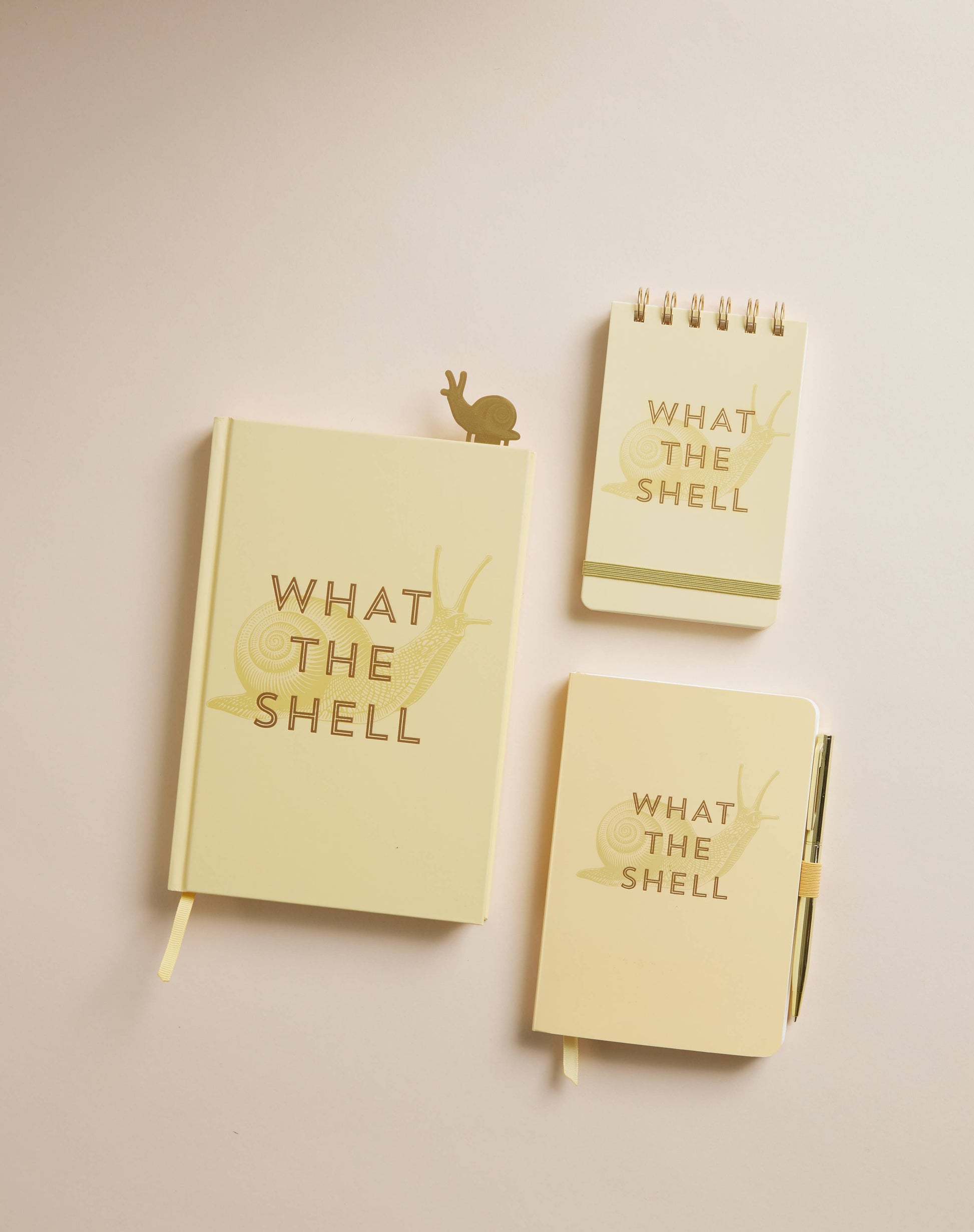 Three light yellow notebooks with 'What The Shell' text on a beige background