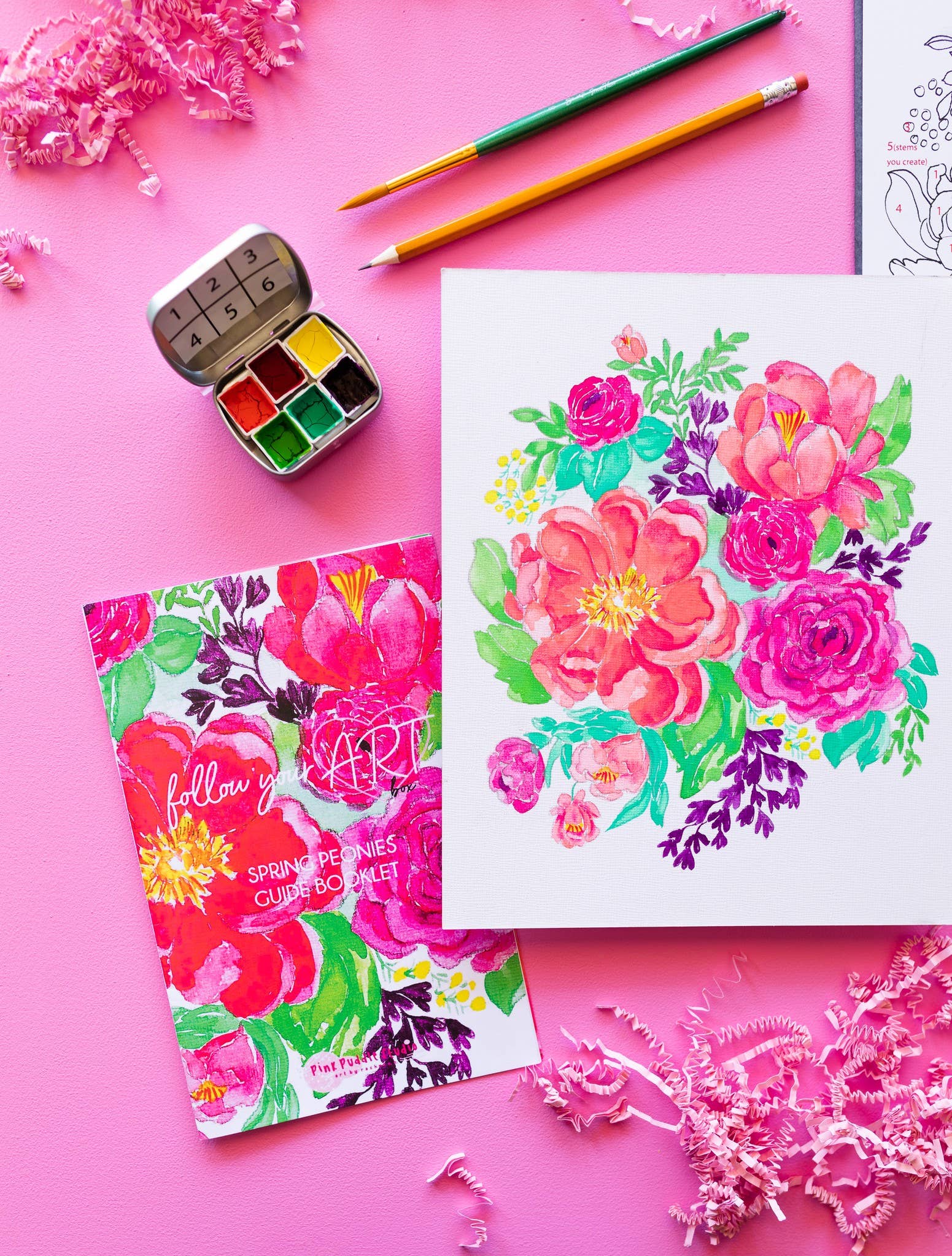 Coloring book with floral design, watercolor painting, and art supplies on a pink background